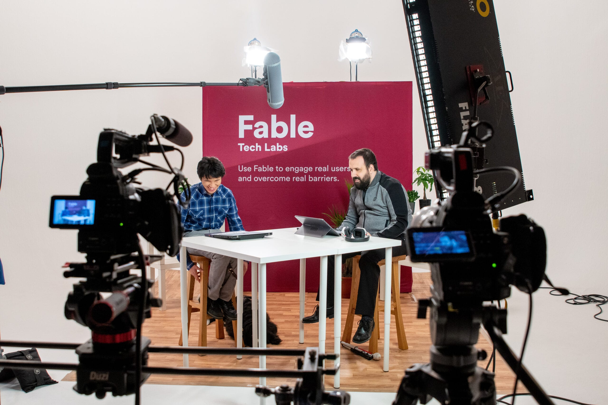 Sam and Ka on set filming for Fable, in a large studio with large lights with a Fable backdrop
