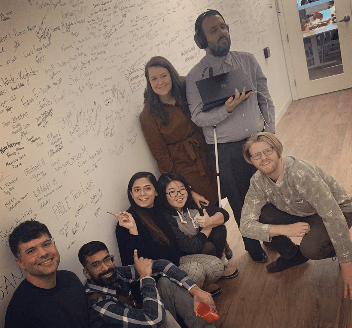 Perry, Abid, Alwar, Minna, Graham, Amber and Sam stand in front of the signature wall at OneEleven, after Fable signed it